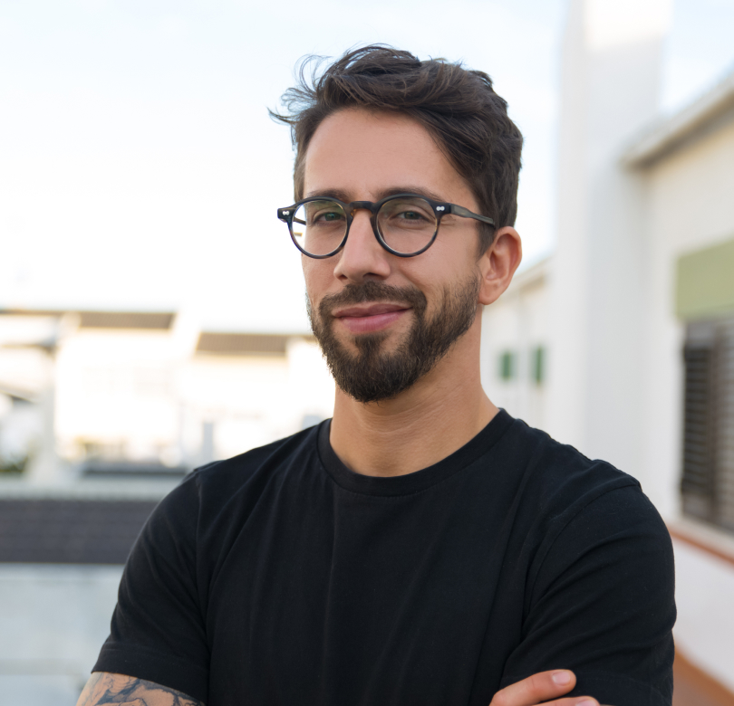 smiling man with dark hair and beard wearing glasses, in a black shirt